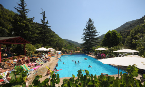 Piscina al aire libre con tumbonas y sombrillas en Camping Delle Rose, Liguria, Italia, rodeada de montañas.
