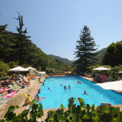 Piscina al aire libre con tumbonas y sombrillas en Camping Delle Rose, Liguria, Italia, rodeada de montañas.