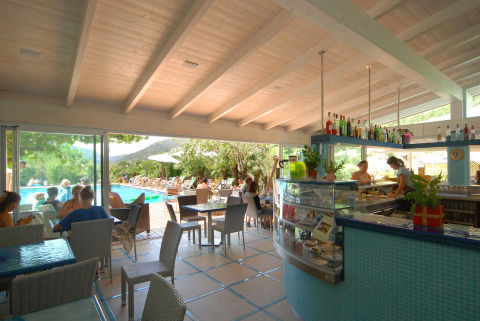 Zona caffè interna con vista sulla piscina, ospiti rilassati al Camping Delle Rose, Liguria, Italia.