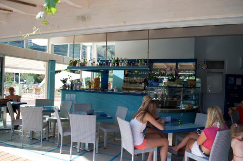 Cafetería interior en Camping Delle Rose en Liguria, Italia, con huéspedes sentados en mesas en un ambiente relajado.