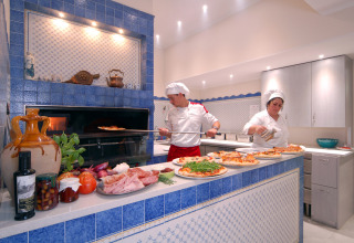 Two chefs preparing pizza at a wood-fired oven in Camping Delle Rose holiday park in Liguria, Italy.