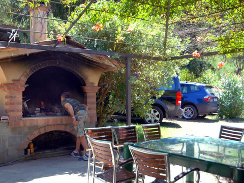 Ein Mann kontrolliert das Essen in einem Steinofen bei Camping Delle Rose, mit Tischen und Autos im Hintergrund.