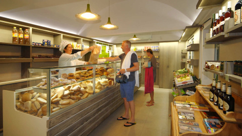 Tienda de comestibles en Camping Delle Rose en Liguria, Italia, con huéspedes comprando pan y alimentos.