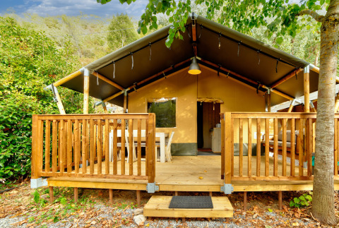 Safarizelt mit Holzveranda im Ferienpark Camping Delle Rose, Ligurien, Italien, umgeben von Bäumen.