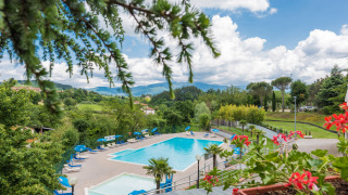 Piscina con lettini prendisole e vista panoramica sulla Toscana al Camping Il Poggetto, Italia.