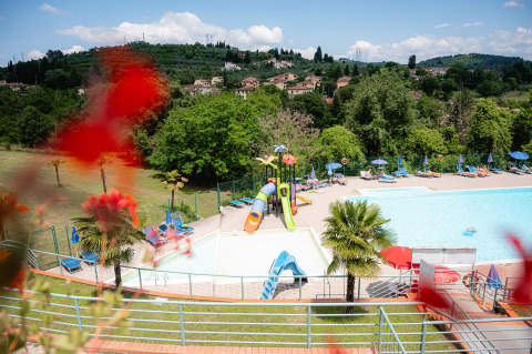 Vista de la piscina y toboganes en Camping Il Poggetto, Toscana, Italia, con colinas al fondo y tumbonas alrededor.