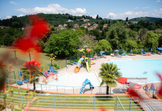Zicht op het zwembad en glijbanen van Camping Il Poggetto in Toscane, Italië, met heuvels op de achtergrond.