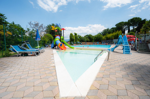Piscina para niños con toboganes y tumbonas en el Camping Il Poggetto, parque vacacional en la Toscana, Italia.