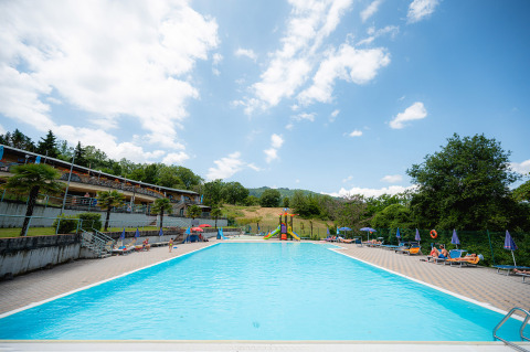 Piscina al aire libre con tumbonas y sombrillas en Camping Il Poggetto, parque vacacional en la Toscana, Italia.