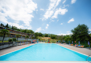 Piscina all'aperto con lettini e ombrelloni al Camping Il Poggetto, parco vacanze in Toscana, Italia.