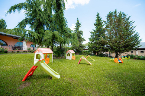 Parque infantil con toboganes de plástico y casitas en el césped de Camping Il Poggetto, Toscana, Italia.