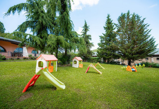 Speelplein met plastic glijbanen en speelhuisjes op gras bij Camping Il Poggetto in Toscane, Italië.