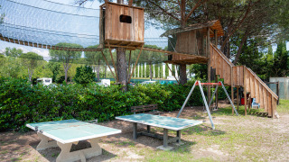 Zona de juegos con casa en el árbol, mesa de ping pong y columpio en Camping Il Poggetto, Toscana, Italia.