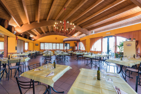 Bright, spacious restaurant with yellow tablecloths and wooden ceiling at Camping Il Poggetto in Tuscany, Italy.