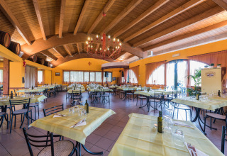 Ristorante luminoso e spazioso con tovaglie gialle e soffitto in legno al Camping Il Poggetto in Toscana, Italia.