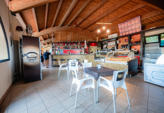 Café intérieur avec plafond en bois, tables et comptoir à glace au Camping Il Poggetto en Toscane, Italie.