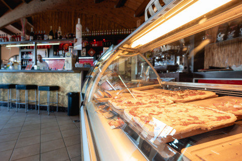 Vista interior de una pizzería en Camping Il Poggetto, pizzas frescas expuestas en vitrina en la Toscana.