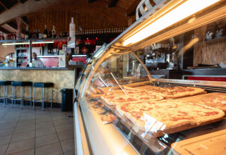 Binnenzicht van een pizzeria bij Camping Il Poggetto, verse pizza’s in een toonbank in Toscane.