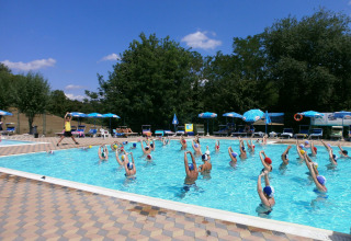 Groep mensen volgt aquagym in het zwembad van Camping Il Poggetto in Toscane, Italië, bij zonnig weer.