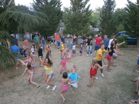 Bambini e adulti che ballano e si divertono all’aperto sul prato al Camping Il Poggetto in Toscana.