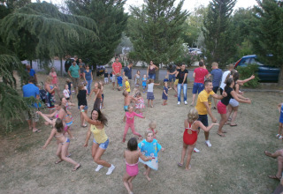 Bambini e adulti che ballano e si divertono all’aperto sul prato al Camping Il Poggetto in Toscana.