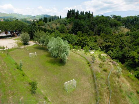 Pequeño campo de fútbol con árboles y porterías en Camping Il Poggetto en la Toscana, Italia, rodeado de colinas.