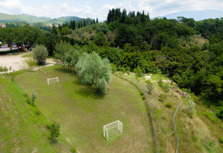Pequeño campo de fútbol con árboles y porterías en Camping Il Poggetto en la Toscana, Italia, rodeado de colinas.