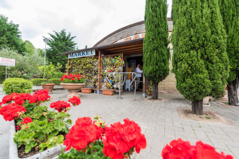 Ingresso del market con fiori colorati e cipressi al Camping Il Poggetto, in Toscana, Italia.