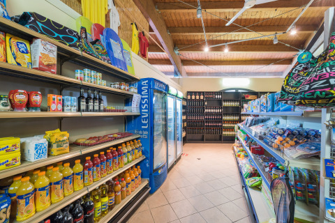 Minimarket del Camping Il Poggetto in Toscana con bevande, cibo e giochi da spiaggia sugli scaffali.