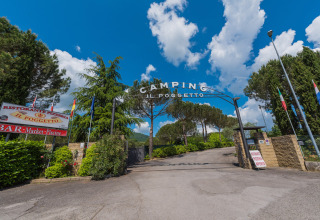 Ingang van Camping Il Poggetto, een vakantiepark in Toscane, Italië, tussen bomen en blauwe lucht.