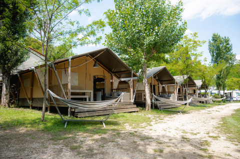 Fila di tende glamping con amache al Camping Il Poggetto, parco vacanze immerso nella Toscana, Italia.