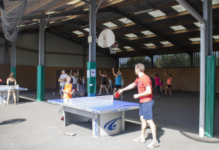 Kinder und Erwachsene spielen Tischtennis und Basketball in einer überdachten Sportanlage im Ferienpark.