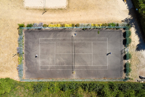 Aerial view of a tennis court at Camping La Bretonnière, Pays de la Loire, France, with two people playing.