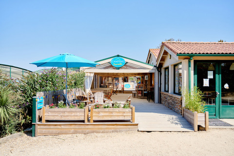 Entrada de Camping La Bretonnière en Pays de la Loire, Francia, con asientos exteriores y sombrilla azul.