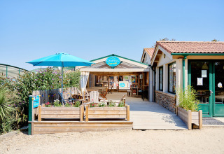 Entrée du Camping La Bretonnière en Pays de la Loire, France, avec terrasse extérieure et parasol bleu.