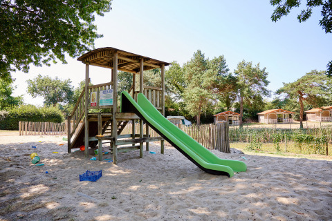 Speelplein met groene glijbaan en houten speelhuis op zand bij Camping La Bretonnière, Pays de la Loire.