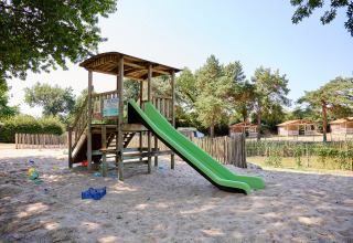 Parco giochi con scivolo verde e struttura in legno sulla sabbia al Camping La Bretonnière, Pays de la Loire, Francia.