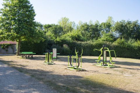 Outdoor gym equipment and picnic table on grassy area at Camping La Bretonnière, Pays de la Loire, France.
