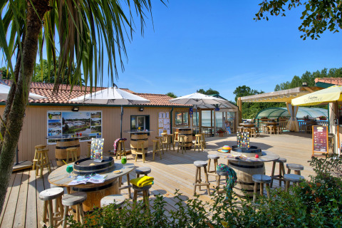 Outdoor terrace at Camping La Bretonnière in Pays de la Loire, France, with tables, umbrellas, and lush greenery.