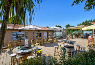 Outdoor terrace at Camping La Bretonnière in Pays de la Loire, France, with tables, umbrellas, and lush greenery.