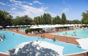 Camping La Chiocciola in Toscana, Italia, con piscine, ombrelloni bianchi e ospiti che si rilassano al sole.