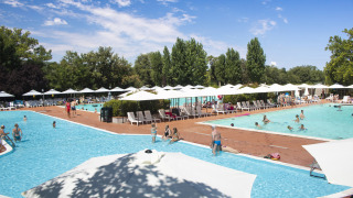 Camping La Chiocciola in Toscana, Italia, con piscine, ombrelloni bianchi e ospiti che si rilassano al sole.