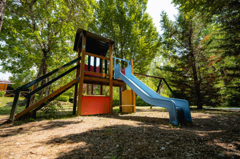 Parque infantil con tobogán y estructura para trepar en Camping La Chiocciola, rodeado de árboles en la Toscana, Italia.