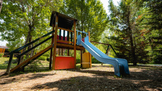 Parque infantil con tobogán y estructura para trepar en Camping La Chiocciola, rodeado de árboles en la Toscana, Italia.