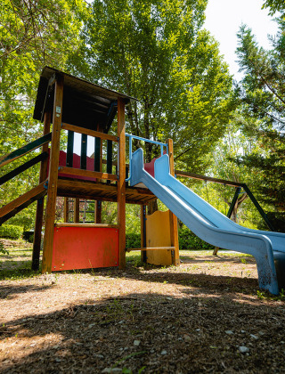 Spielplatz mit Rutsche und Kletterturm im Grünen des Ferienparks Camping La Chiocciola in der Toskana, Italien.
