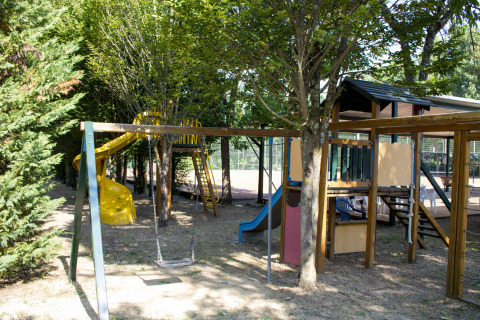 Speeltuin met schommels, glijbanen en klimrek onder bomen bij Camping La Chiocciola in Toscane, Italië.