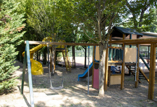 Parque infantil con columpios, toboganes y estructura de juego bajo árboles en Camping La Chiocciola, Toscana, Italia.