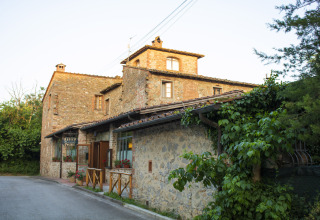 Edificio in pietra immerso nel verde al Camping La Chiocciola, parco vacanze in Toscana, Italia, al tramonto.