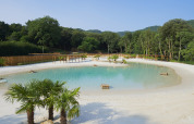 Camping La Clémentine en Occitania, Francia, con una laguna artificial, playa de arena y vegetación.