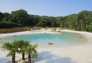 Camping La Clémentine en Occitania, Francia, con una laguna artificial, playa de arena y vegetación.